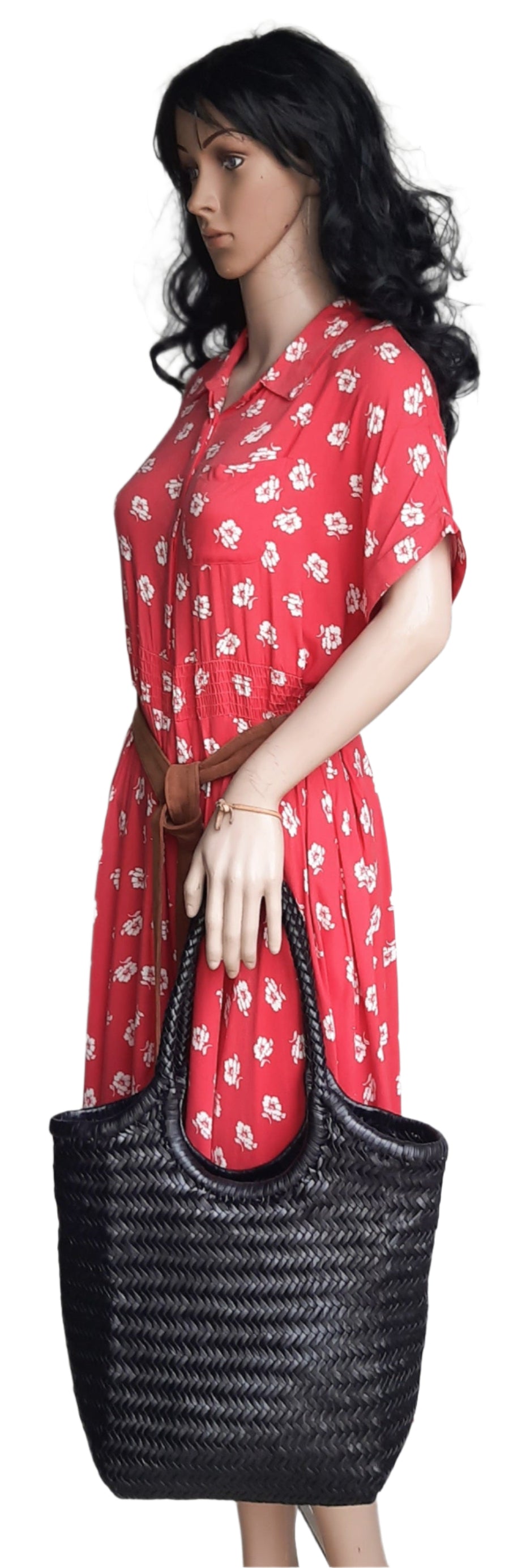 Woman wearing a red floral dress holding a black woven bag against a white background